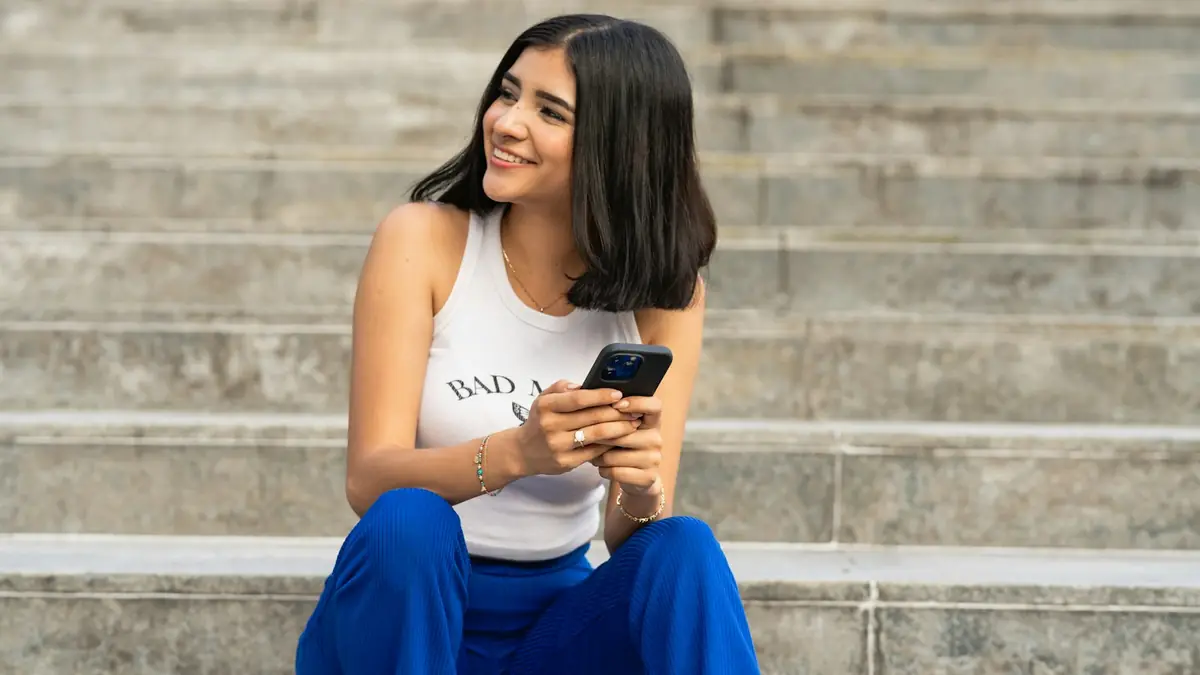 Mujer sonriente sentada en unas escaleras mirando su teléfono