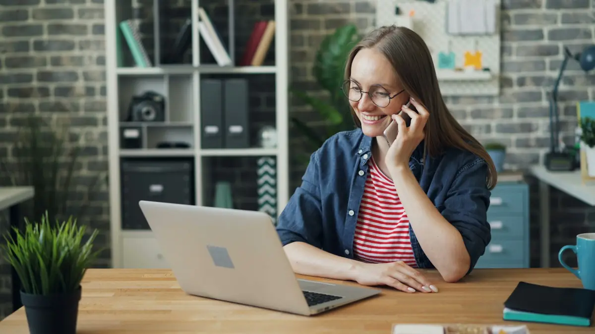 Vendedora hablando por teléfono mientras revisa su portátil