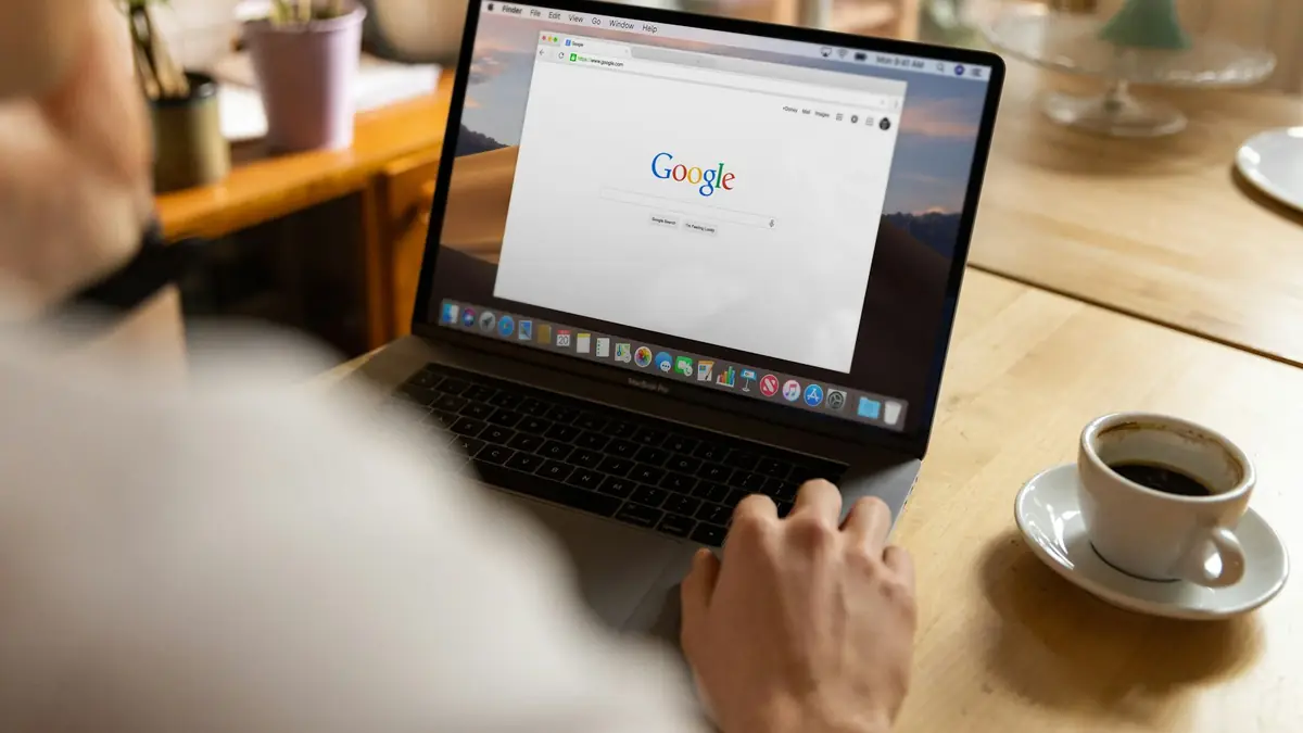 Persona buscando en Google desde su portátil junto a una taza de café