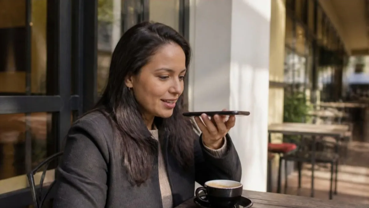 Mujer latina en un café haciendo una pregunta a un asistente de IA desde su celular