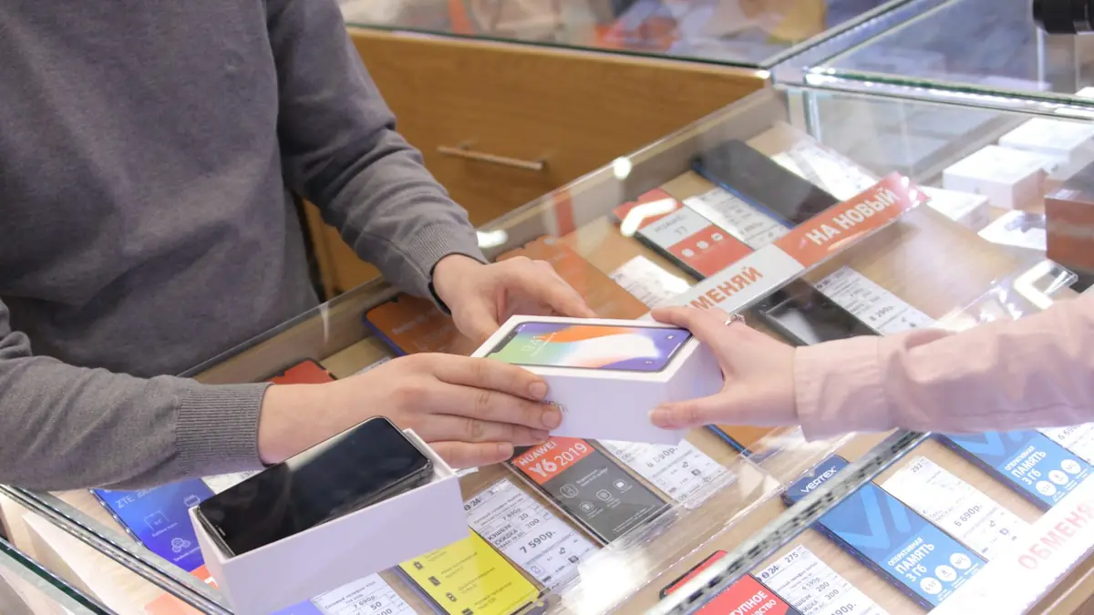 Vendedor mostrando un teléfono a una clienta en el mostrador de una tienda